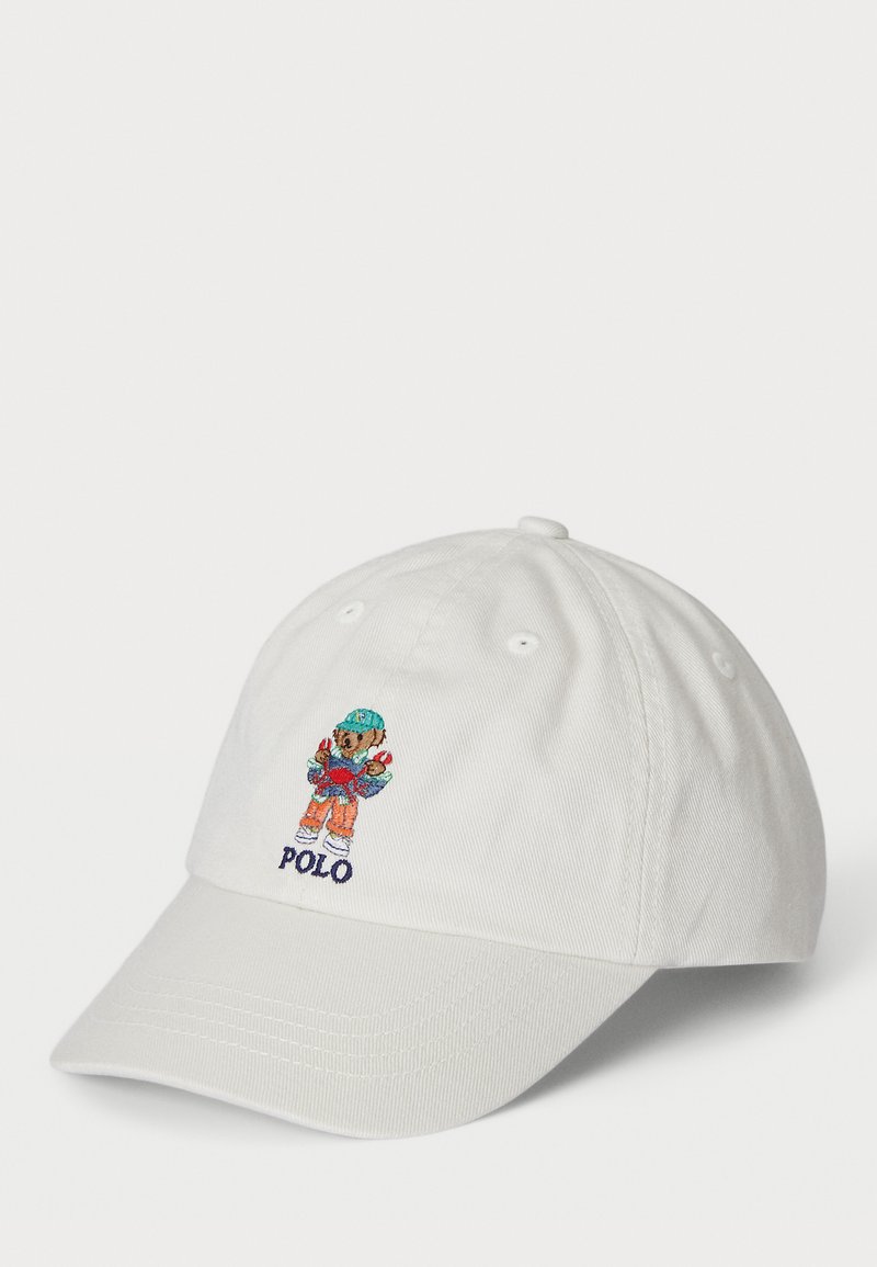 Bílá bavlněná čepice s barevným vyšitým motivem postavy a textem "POLO" vpředu, s prohnutým kšiltem a nastavitelným páskem na zadní straně.