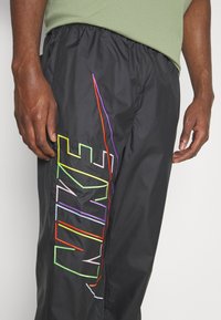 Svarta nylonbyxor med djärv flerfärgad "NIKE" logotyp broderi, elastisk midja och lös passform. Texturen är mjuk och lätt.