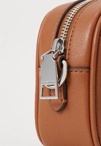 Primo piano di una borsa in finta pelle marrone, con zip e componenti in argento. Texture liscia con dettagli di cucitura lungo i bordi.