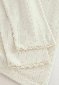 Knitted fabric in cream color with vertical stripes. Features a delicate lace trim and small diamond patterns throughout. Soft texture.
