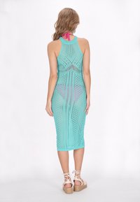 O rochie croșetată turcoaz, cu o siluetă ajustată, design cu spatele în formă de brad și tiv la genunchi. Accentuata cu o fundă roz la gât.