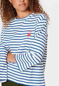 Pasiasta, długi rękaw koszula w białym i niebieskim kolorze z okrągłym dekoltem, z czerwonym haftowanym detalem w kwiaty na piersi.