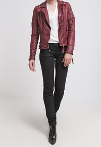 Bordeauxrode leren bikerjack met ritssluitingen in de zakken, gecombineerd met een witte blouse en zwarte skinny jeans. Model draagt zwarte, spits toelopende enkellaarsjes.