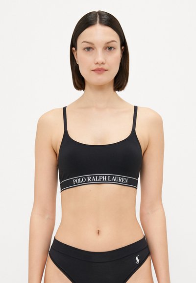 Bralette noire avec des bretelles fines, arborant une bande blanche « POLO RALPH LAUREN ». Texture mate et design simple et ajusté.