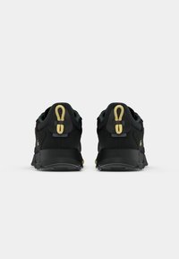 Pair of black athletic shoes with yellow pull tabs and Lacoste logo viewed from the back on a white background.