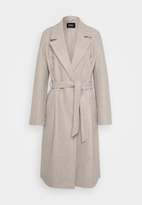 Lys beige lang ullkåpe for kvinner med brede revers og et stoffbelte knyttet i midjen på hvit bakgrunn.