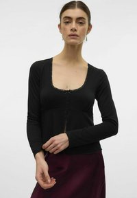 Svart långärmad topp med spetskant längs halslinningen, med en V-formad utskärning och rak passform, i kombination med en vinröd kjol.