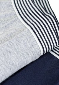 Tessuto in misto cotone di colore grigio chiaro e blu navy, dotato di una cintura elastica a righe nere e bianche, caratterizzato da una texture morbida e una finitura liscia.