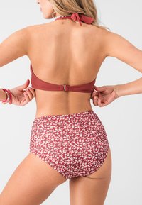 Červený bikiny top s krkem na zavazování a sponou na zádech, spárovaný s vysokými kalhotkami s květinovým potiskem v bílé a modré barvě.