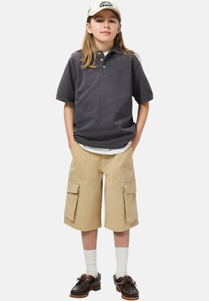 Camiseta polo gris de manga corta, pantalones cortos cargo beige con bolsillos delanteros, calcetines blancos y zapatos marrones. Sombrero con logo en la parte delantera.