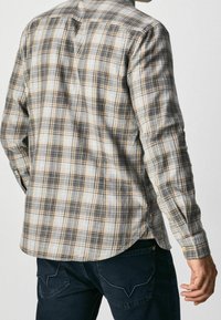 Camicia a maniche lunghe a quadri grigi con accentuazioni arancioni, polsini con bottoni e orlo curvo. Realizzata in tessuto leggero; dettagli di cucitura visibili.