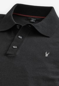 Zwarte polo gemaakt van gebreide stof met een gestructureerde kraag, drie donkere knopen en een klein geborduurd hertlogo op de borst.