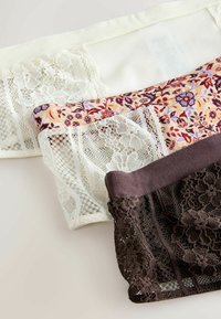 Három pár női fehérnemű: fehér csipkével, virágmintás és barna csipke. Mindegyik bonyolult mintákkal és eltérő textúrákkal rendelkezik.