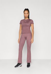 Σκούρο μωβ αθλητική σειρά που περιλαμβάνει κορυφαία κοντομάνικη φανέλα και φαρδιά παντελόνια, φτιαγμένα από ελαστικό υλικό, με ένα μικρό λευκό λογότυπο σε κάθε κομμάτι.