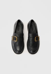 Black leather loafers with a wide strap and gold metal buckle accent. Smooth texture, rounded toe, subtle stitching detail, and rubber sole.