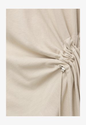 Krämfärgad tyg som är rynkad och åtdragen med en silverfärgad metallkordlåsmekanism på en dragsnodd.