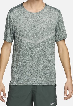 Mand iført en kortærmet grå tekstureret sportstrøje og mørkegrønne shorts med Nike-logo på begge beklædningsgenstande.