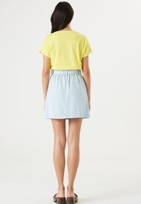 Gul bomullströja med uppvikta ärmar, parat med en ljus denim A-linjeformad kjol som har en bälte i midjan och en avslappnad passform.