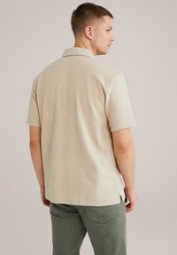 Bežna srajca s kratkimi rokavi z navpičnimi črtami, ki ima koničast ovratnik in ravno rob z stranskimi razporki. Narejena iz mehkega blaga.