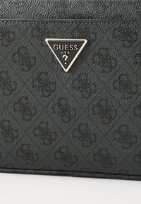 Portafoglio nero texture con motivo in rilievo e logo triangolare dorato con la scritta "GUESS USA." Finitura liscia con una leggera lucentezza.