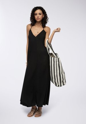 Vestito lungo senza maniche di colore nero con scollatura a V, abbinato a una borsa a strisce in crema e nero. Modella che indossa sandali piatti con cinturini.