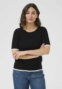 Černý krátký rukáv top s kulatým výstřihem. Obsahuje kontrastní bílé lemy na rukávech a spodním okraji, vyrobený z měkké texturované tkaniny.