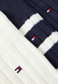 Knit sweater in navy and white featuring ribbed texture, horizontal stripes, and a small embroidered logo in red, white, and blue.