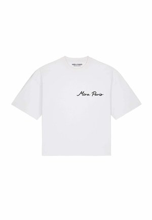 Homme portant des lunettes de soleil et un t-shirt blanc avec un dessin abstrait en ligne noire de deux visages dans le dos, debout dans une rue de la ville.