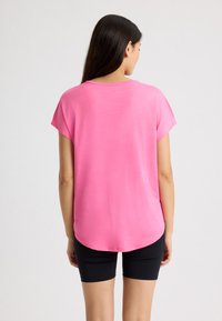 Top rosa a maniche corte con orlo arrotondato, realizzato in tessuto leggero, abbinato a pantaloni shorts neri aderenti, che mostrano una texture liscia.