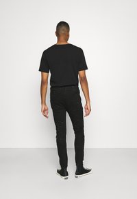 Camiseta negra de manga corta, combinada con jeans skinny negros con detalles desgastados. Llevada con zapatillas altas negras.