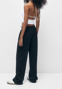 Haut halter blanc avec des bretelles croisées dans le dos, assorti à un pantalon noir ample et des baskets blanches avec des accents gris.