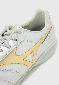 Pantofii sport argintii �și aurii, cu un superior din piele, prezentând o textură netedă, detalii cusute și o guleră căptușită.