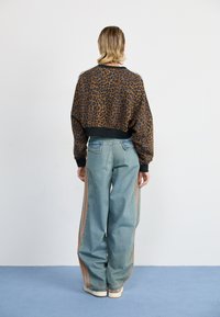 Bruine panterprint cropped sweatshirt met zwarte boorden, gecombineerd met losse lichtblauwe jeans met oranje zijkanten. Witte sneakers.