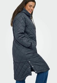 Tmavě šedý prošívaný puffer kabát s vysokým límcem, kapucí na stahovací šňůrku a postranními patentkami. Obsahuje strukturovaný diamantový vzor a postranní kapsy.