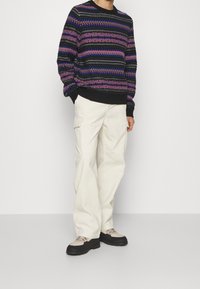 Neulepaita mustana, purppurana ja sinisenä geometrisin kuvioin; yhdistettynä vaaleanbeigeihin cargo-housuihin ja tukeviin musta-harmaisiin kenkiin.