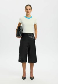 Chemise blanche à manches courtes avec un col bleu clair, associée à des culottes en cuir noir et des talons pointus noirs ; tenant un sac fourre-tout noir.
