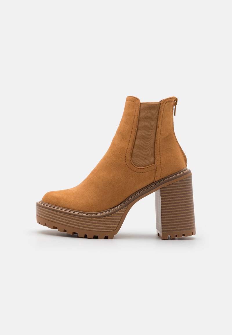 Šedohnědé vysoké boty s podpatkem po kotníky, zaoblenou špičkou, texturovaným semišovým materiálem, elastickými bočními panely a robustní platformou s vroubkovaným vzorem.