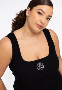 Zwarte geribbelde tanktop met een brede halslijn, dikke banden en geborduurd logo op de borst. Vlotte textuur en aansluitend ontwerp.