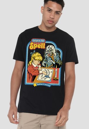 Junges Mädchen mit blondem Haar zeigt auf Buchstaben eines Ouija-Brettes, während eine geisterhafte Gestalt im Hintergrund auftaucht; Text lautet "Lerne zu buchstabieren".