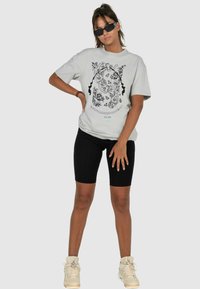 Lys grå t-shirt med sort blomstermotiv, parret med sorte cykelshorts og beige sneakers. Glat bomuldsstof.