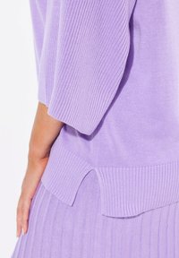 Top in lavanda lavorato a maglia, con texture a coste, maniche corte e design con orlo spaccato per un effetto a strati. Tessuto morbido e leggero.