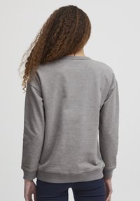 Felpa grigia con collo tondo, polsini e orlo a costine. Tessuto morbido, vestibilità rilassata e materiale più leggero senza pattern o dettagli visibili.
