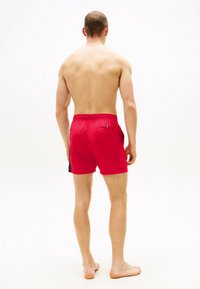 Shorts de bain rouges avec un panneau latéral noir, taille élastique et poche arrière. Tissu léger avec une texture lisse.