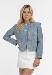Blauw gestreepte, textuurjacket met een ronde hals, drie knopen en lange mouwen. Draag het over een witte rok met een licht verkort ontwerp.