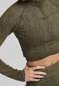 Top sportivo accollato a zip e maniche lunghe di colore verde oliva, con un motivo testurizzato e il logo PUMA sul petto. Tessuto liscio al tatto.