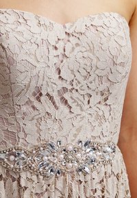Strapless lace dress in beige, featuring floral patterns and a beaded waistband with pearls and crystals for detailing.