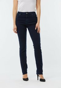 Jeans taille haute bleu foncé avec une coupe slim, dotés d'une fermeture à bouton, de cinq poches et de détails de couture subtils.