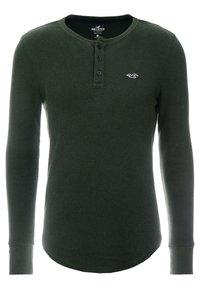 Camisa henley de manga larga verde, hecha de una tela texturizada, con una tapeta de tres botones y un pequeño logo en el pecho.