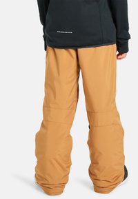 Vodotesné béžové snehové nohavice s voľným strihom, spevnenými švami a jemnými čiernymi akcentmi na páse. Elastické manžety na zabezpečenie pohodlného fitu.