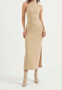 Beige ribbed knit halter neck dress with bodycon fit and knee-high side slit, paired with beige fitted ankle boots.